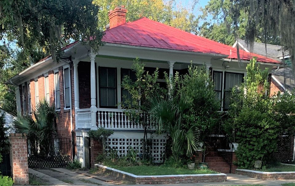 Raised brick house with a red metal hip roof, white porch columns and palmettos