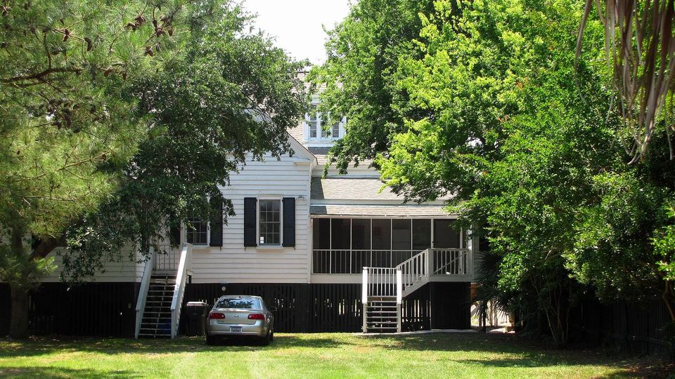 White clapboard house raised on a high foundation with outside stairs and a screened porch