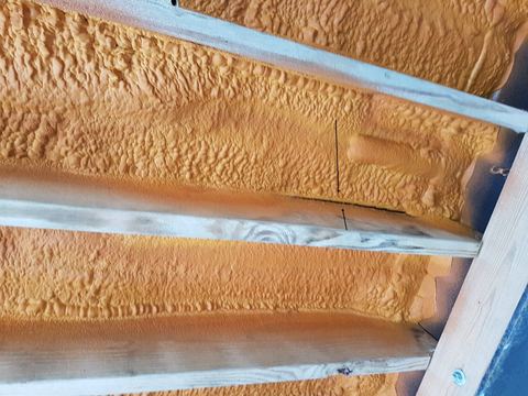 Orange spray foam insulation filling the bays between wooden rafters on a roof deck